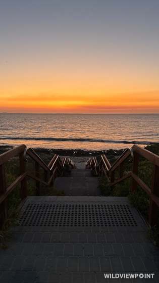The same kind of stairway to the beach in deep orange afterglow, a ship on the horizon and small waves along the shore.